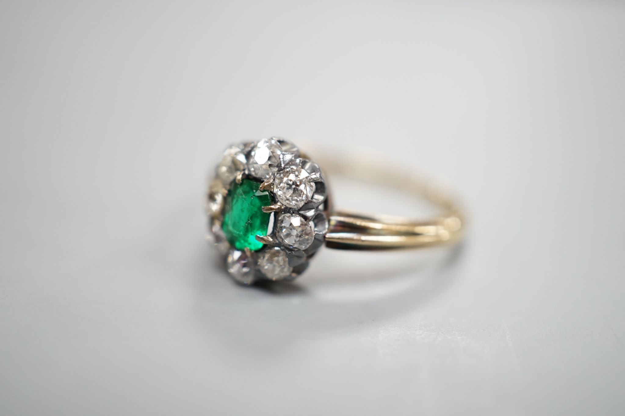 A yellow metal, emerald and diamond set oval cluster ring, size M/N, gross weight 3.1 grams.